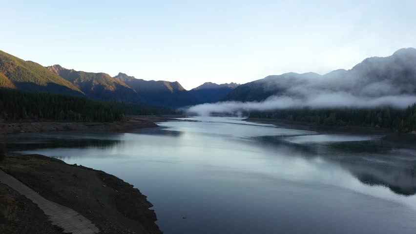 4K aerial drone footage of sunrise at Wynoochee Lake dam in Olympic National Forest, Washington State, USA, showing calm water, low clouds, and forested mountain landscape in peaceful morning 