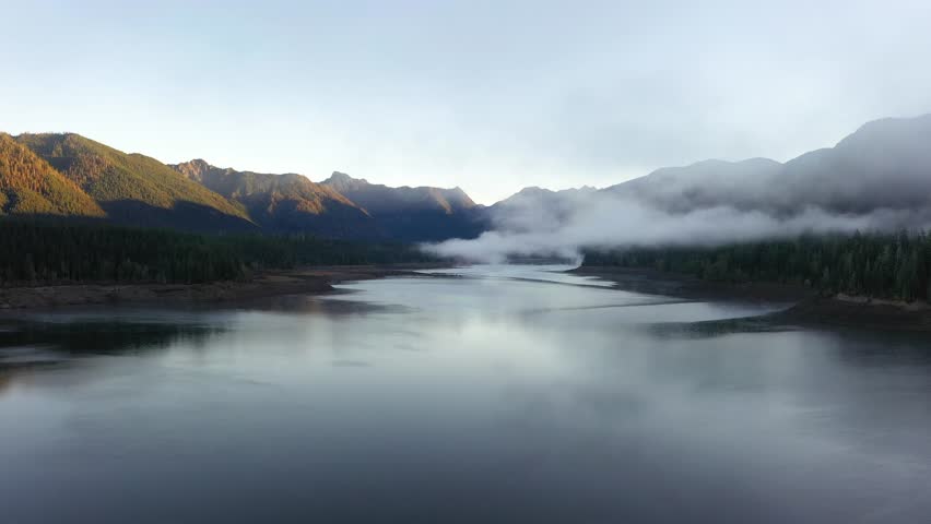 4K aerial drone footage of sunrise at Wynoochee Lake dam in Olympic National Forest, Washington State, USA, showing calm water, low clouds, and forested mountain landscape in peaceful morning 