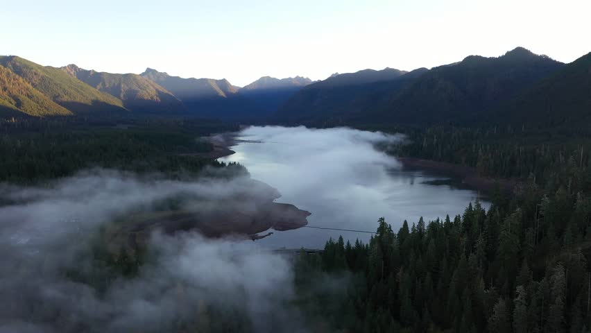 4K aerial drone footage of sunrise at Wynoochee Lake dam in Olympic National Forest, Washington State, USA, showing calm water, low clouds, and forested mountain landscape in peaceful morning 