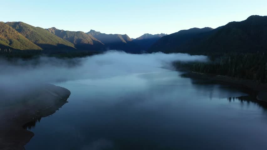 4K aerial drone footage of sunrise at Wynoochee Lake dam in Olympic National Forest, Washington State, USA, showing calm water, low clouds, and forested mountain landscape in peaceful morning 
