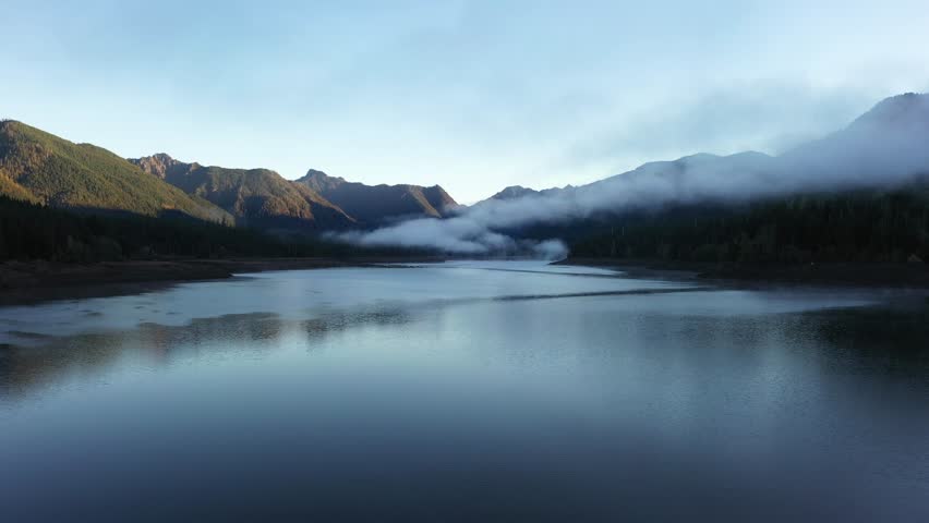 4K aerial drone footage of sunrise at Wynoochee Lake dam in Olympic National Forest, Washington State, USA, showing calm water, low clouds, and forested mountain landscape in peaceful morning 