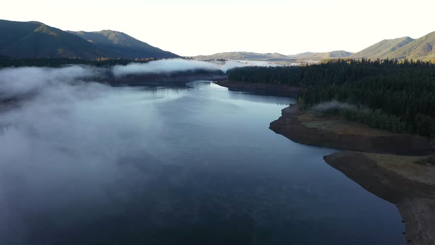 4K aerial drone footage of sunrise at Wynoochee Lake dam in Olympic National Forest, Washington State, USA, showing calm water, low clouds, and forested mountain landscape in peaceful morning 