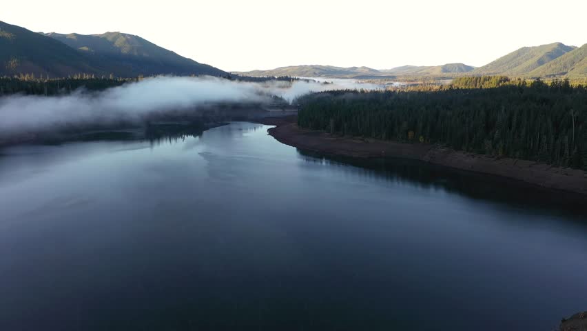 4K aerial drone footage of sunrise at Wynoochee Lake dam in Olympic National Forest, Washington State, USA, showing calm water, low clouds, and forested mountain landscape in peaceful morning 