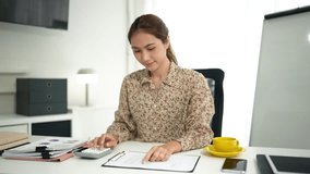 Focused Asian adult woman diligently performing financial analysis and strategic business planning with calculator documents in a bright home office setting - Powered by Shutterstock - Get 15% off with code: PIKWIZARD15