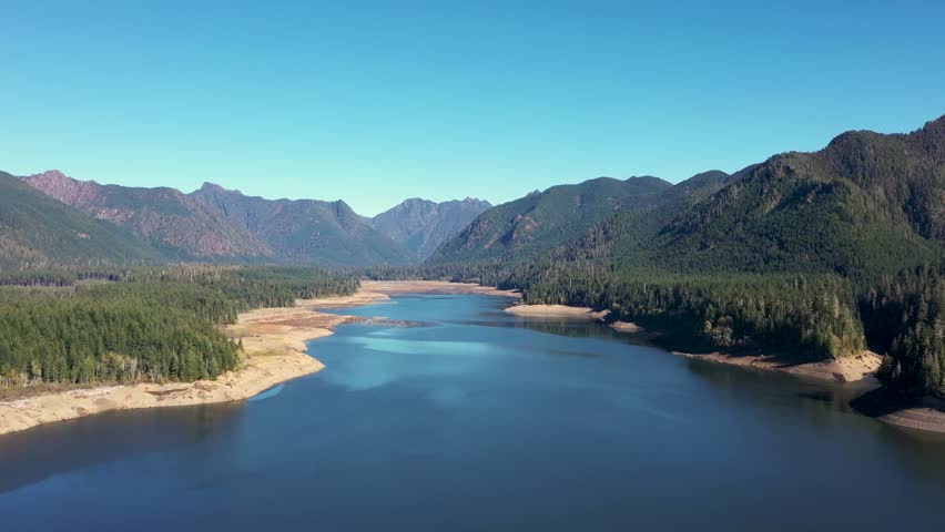 4K aerial drone footage of Wynoochee Lake dam in Olympic National Forest, Washington State, USA, showing clear blue water surrounded by evergreen forests and mountains under bright daylight, clear sky
