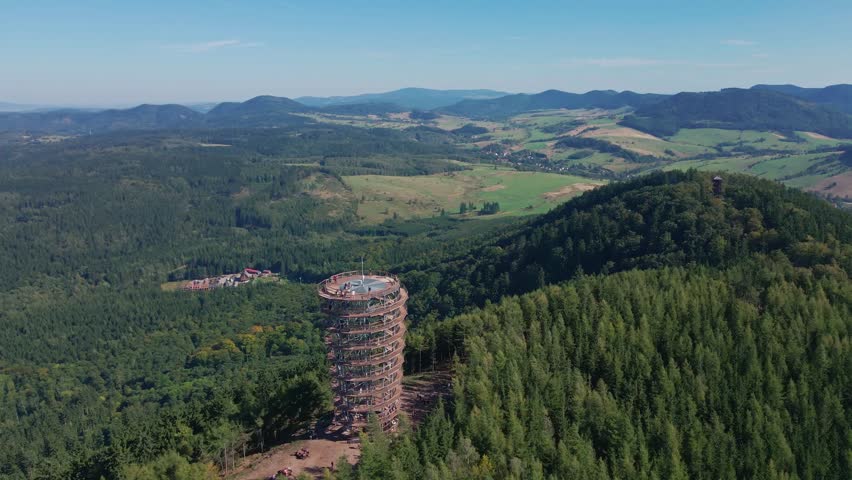 Aerial panoramic view of observation tower on forested mountain hill. Natural vast landscape with forest and distant ridges