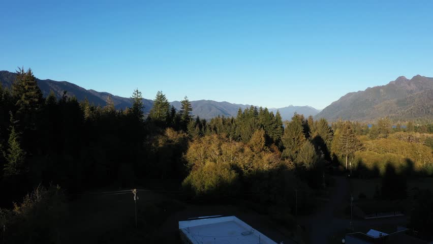 4K aerial drone footage of Quinault Lake in Olympic National Park, Washington State, USA, showing golden sunset light over calm blue water surrounded by evergreen forests and mountain landscape