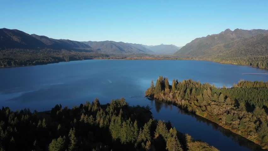 4K aerial drone footage of Quinault Lake in Olympic National Park, Washington State, USA, showing golden sunset light over calm blue water surrounded by evergreen forests and mountain landscape