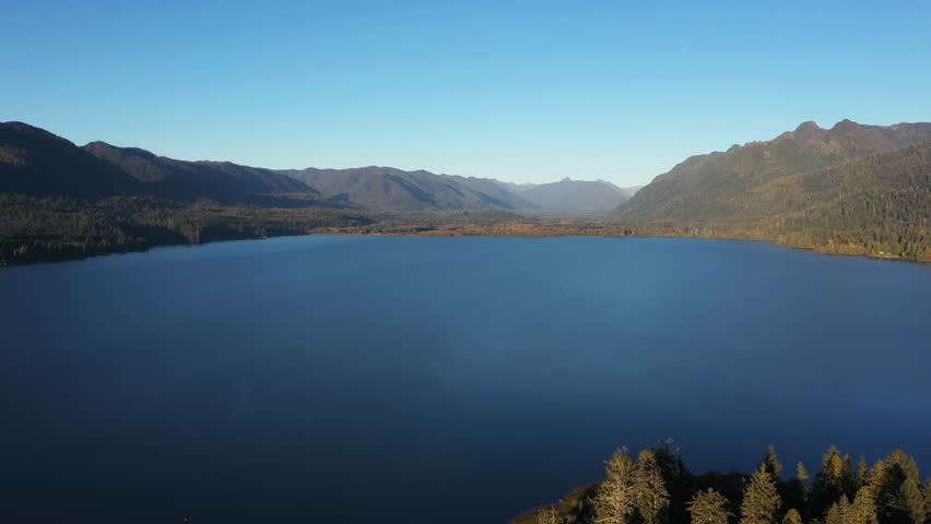 4K aerial drone footage of Quinault Lake in Olympic National Park, Washington State, USA, showing golden sunset light over calm blue water surrounded by evergreen forests and mountain landscape