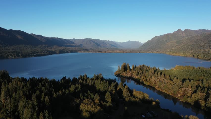 4K aerial drone footage of Quinault Lake in Olympic National Park, Washington State, USA, showing golden sunset light over calm blue water surrounded by evergreen forests and mountain landscape