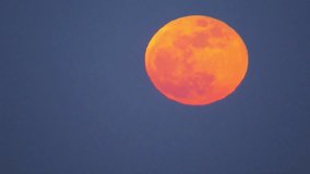 Telephoto static shot of a bright orange-red supermoon at full phase. A small airplane passes across the top, leaving a thin trail that visually cuts through the moon like a line. 2021 - Powered by Shutterstock - Get 15% off with code: PIKWIZARD15