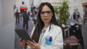 Young chinese woman scientist in a lab coat and protective glasses analyzing data on a tablet outdoors on a bustling street. - Powered by Shutterstock - Get 15% off with code: PIKWIZARD15