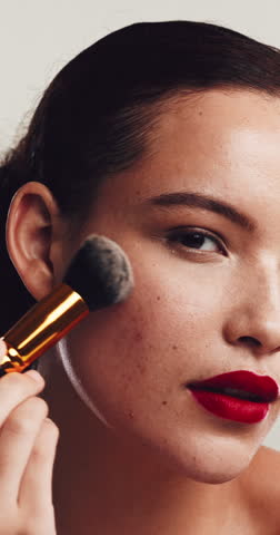 Beauty, blush and face with woman in studio for cosmetics, facial or makeover routine. Apply, freckles and makeup brush with model on white background for aesthetic, change or transformation