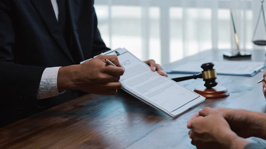Professional lawyer carefully reviewing contract details with client, explaining legal terms and conditions inside modern law firm workspace, preparing for agreement signing
