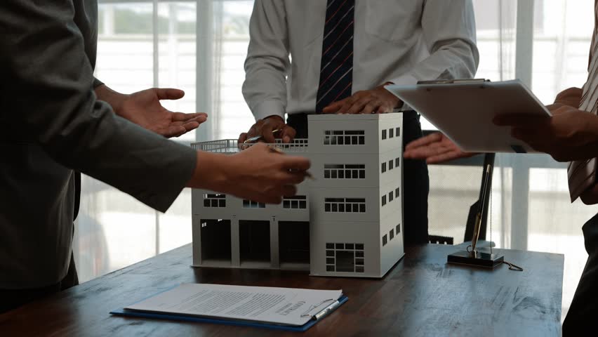 Business professionals collaborating during contract negotiation, reviewing architectural plans and signing agreement for new commercial building development in modern office setting