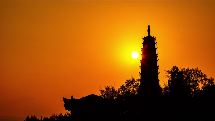 Stunning sunset silhouette of traditional Chinese pagoda tower with golden orange sky backdrop, perfect for travel and cultural themes in Lanzhou region.