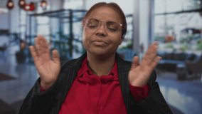 Woman with red hair wearing round glasses and a pinstriped jacket rests cheek on hands inside building lobby; tiredness. - Powered by Shutterstock - Get 15% off with code: PIKWIZARD15