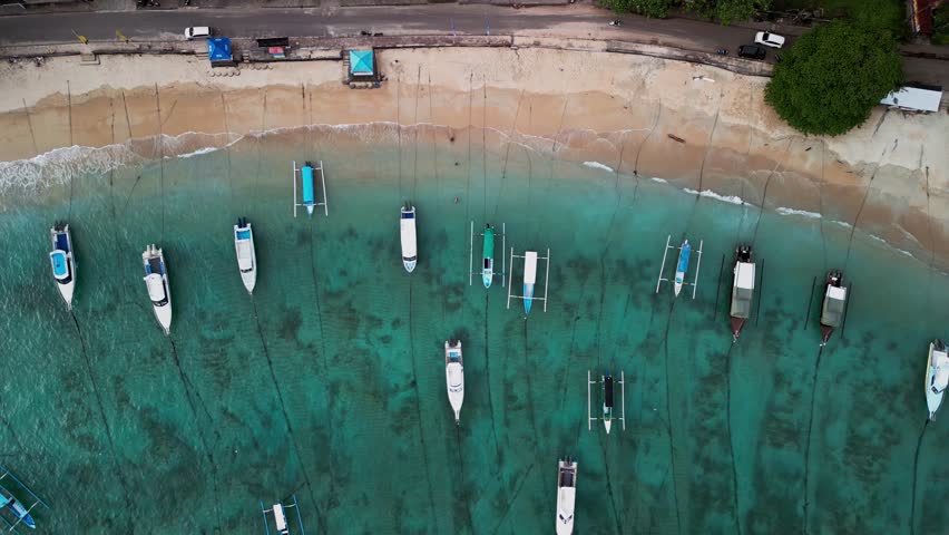 Stunning top down drone view of Padang bai Beach in Bali, where boats rest over turquoise water and golden sand, showcasing the peaceful beauty of this tropical harbor and its coastal charm.