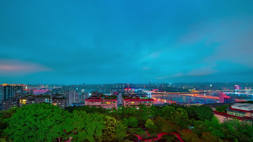 Stunning night time lapse view of illuminated city skyline and bridge across Yangtze River with mountains in background, captured from elevated bank viewpoint in China.
