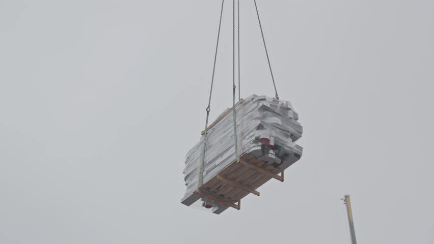 Close up of material being lowered by a crane on a construction site on a cloudy day