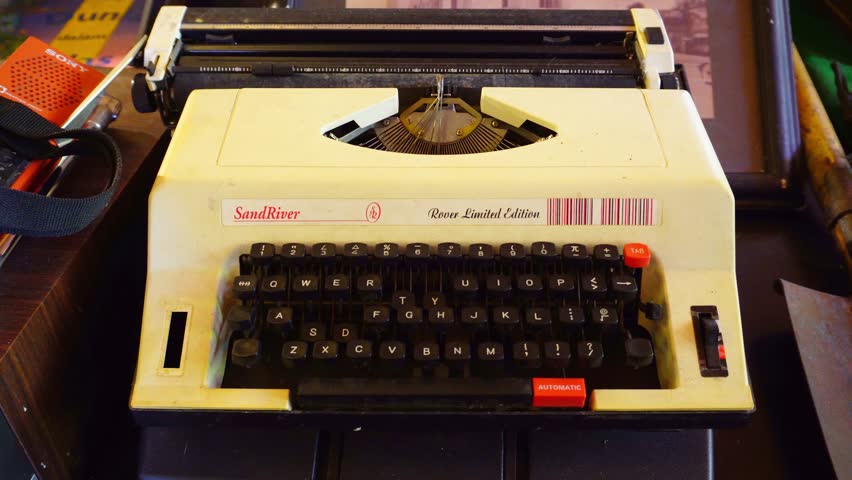 Surakarta, Indonesia - May 18, 2025: A beige and black portable typewriter with the brand "SandRiver". The keyboard is black with red keys. The typewriter is placed on a dark surface.
