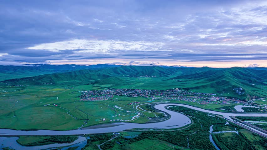 Aerial view of winding river through green grasslands and mountains in Hongyuan, Sichuan Province, China at twilight with dramatic cloudy sky