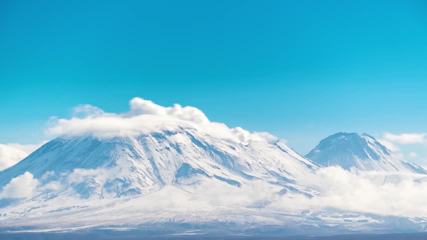 Stunning snow-capped mountain peaks rising above white clouds against brilliant blue sky, perfect for nature and landscape projects showcasing alpine wilderness beauty.