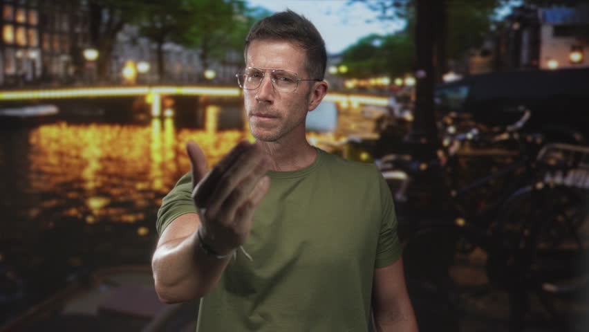 Man gives thumbs up gesture on an amsterdam street at night with canal lights and bicycles visible; confidence travel adventure.
