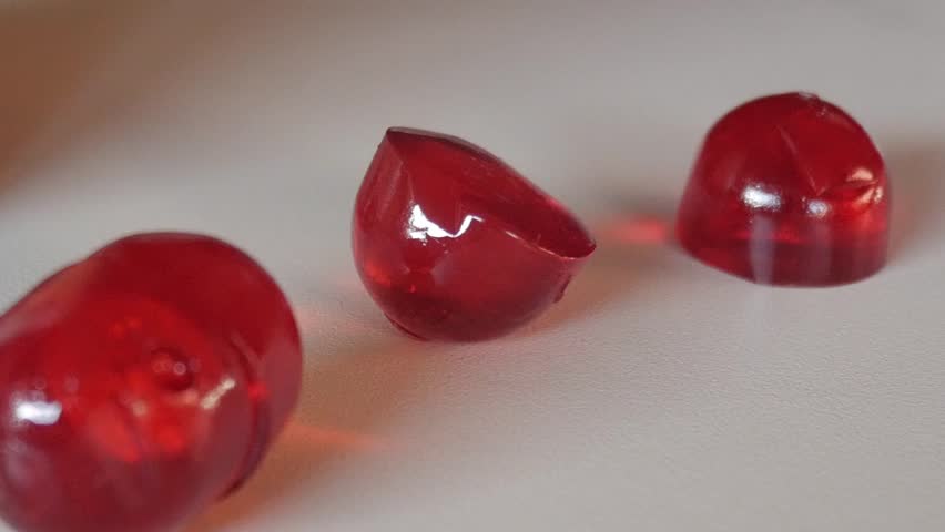 Macro close-up of red vitamin gummies on a white table showing texture and transparency under natural light.