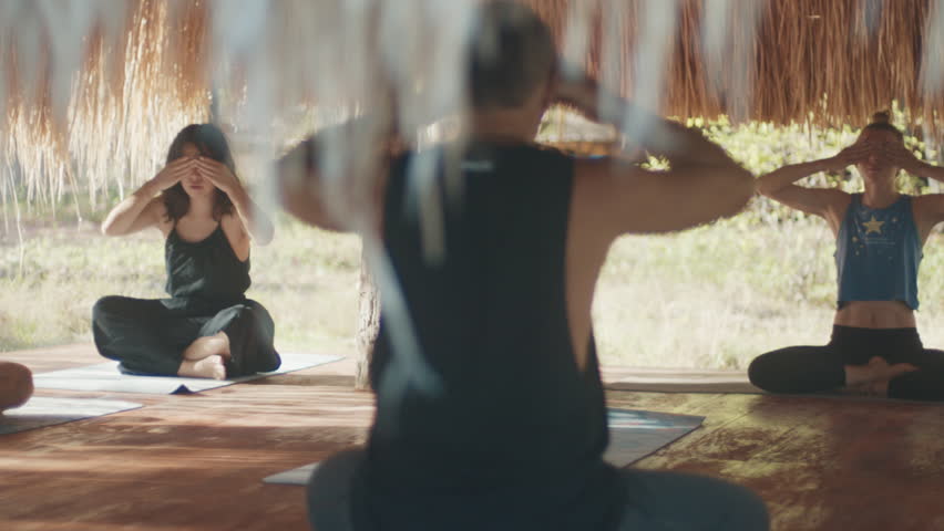 Morning yoga in tropics. Mixed group of people do morning yoga in the tropical outdoor bungalow with straw roof
