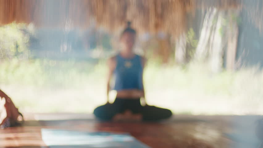 Morning yoga in tropics. Naturally blurred footage of the young woman relaxing during morning yoga in the tropical outdoor bungalow with straw roof