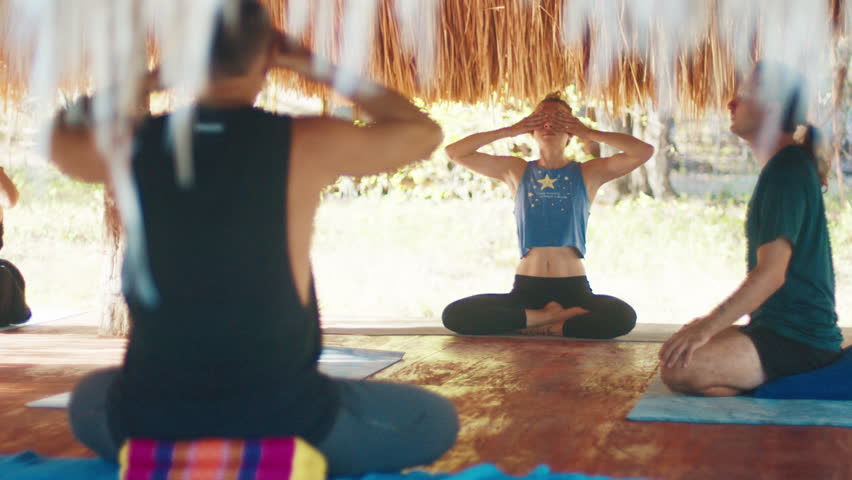 Morning yoga in tropics. Mixed group of people do morning yoga in the tropical outdoor bungalow with straw roof