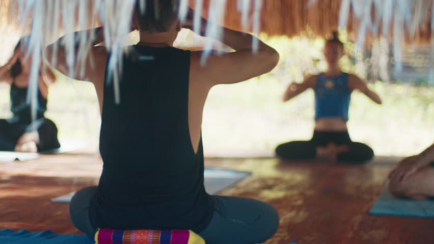 Morning yoga in tropics. Mixed group of people do morning yoga in the tropical outdoor bungalow with straw roof