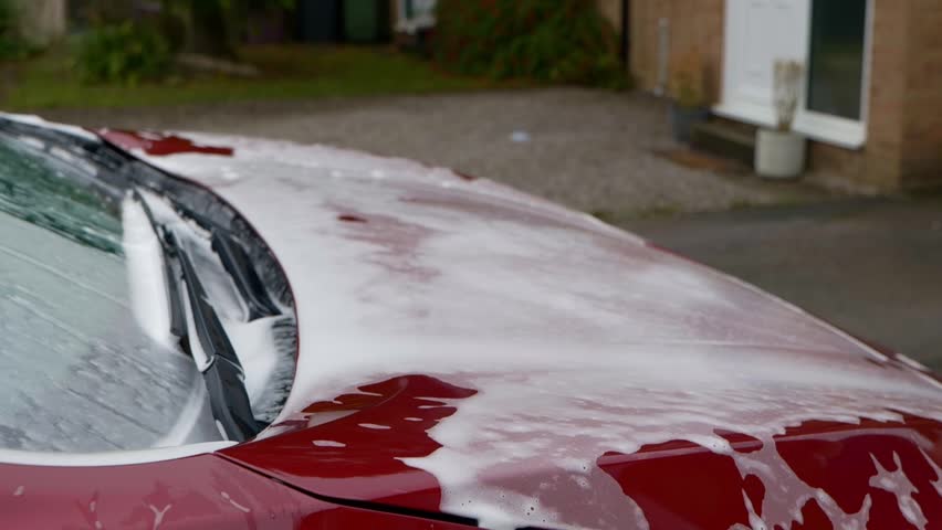 Washing a dark cherry red EV car with snow foam and shampoo with a red microfibre wash mitt - close to camera