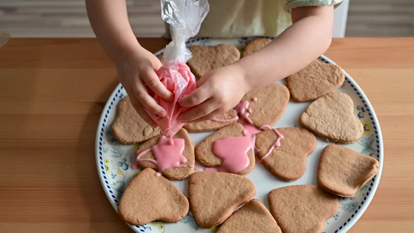 Little toddler girl decorating heart-shaped cookies with pink frosting. Ultra HD 4K video footage
