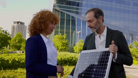 Senior engineer presenting a photovoltaic solar panel to a female colleague outdoors. Professional business partners discussing sustainable and renewable green energy technology for their company - Powered by Shutterstock - Get 15% off with code: PIKWIZARD15