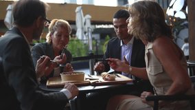 Four mature colleagues in formal attire are enjoying a meal and engaging in conversation while sitting at an outdoor restaurant terrace, fostering teamwork and professional relationships - Powered by Shutterstock - Get 15% off with code: PIKWIZARD15