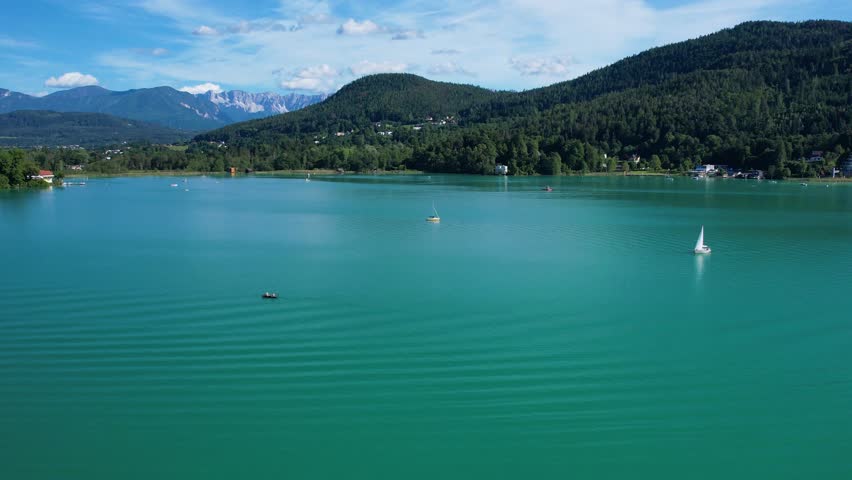 Aerial landscape of Worthersee in Klagenfurt, Austria featuring charming waterfront homes, lush greenery, and serene blue waters under a clear sky.