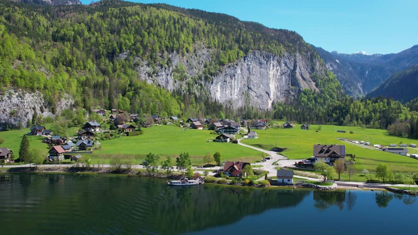 Experience the breathtaking aerial views of Grundlsee Lake in Austria, highlighting the serene waters, green landscapes, and majestic mountains during a clear day.
