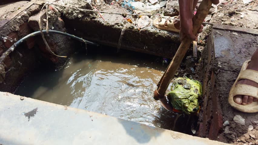 Worker Clears Mud Filled Water Channel by Tool, Manual Cleaning of Clogged Urban Drainage, Debris Removal from Polluted Street Drain, Maintenance for Flooded Sewer Line, Laborer remove Waste from pit