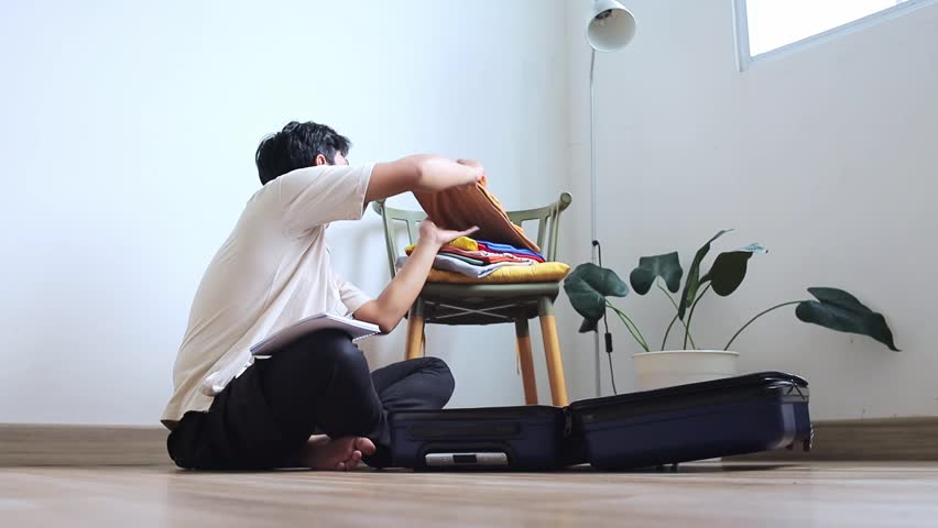 Diligent Young asian man packing suitcase while take notes preparing for journey