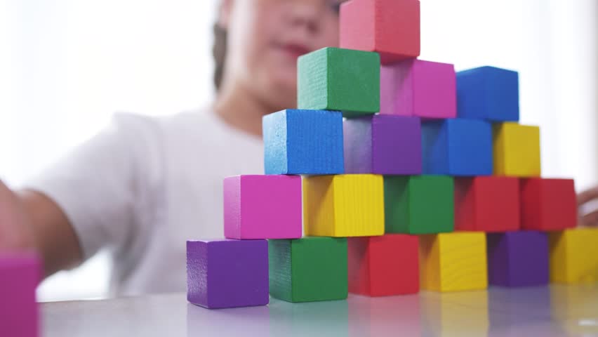 A girl plays with blocks and toys in kindergarten. Constructor little child concept. The girl daughter is playing with cubes. Girl collects lifestyle toys from a stack of cubes.