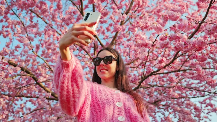 Joyful moment of traveler capturing spring memories among pink cherry flowers