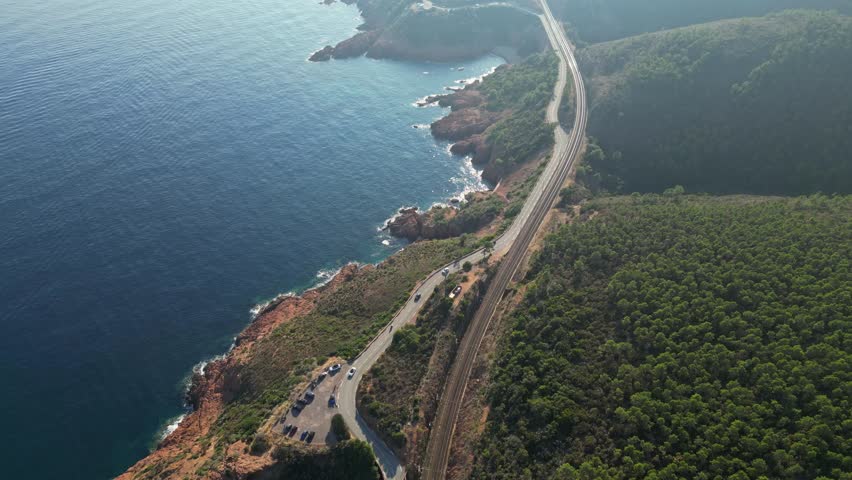 Aerial panoramic view of a winding mountain road along steep cliffs above the turquoise Mediterranean Sea, Esterel Mountains, French Riviera, Southern France – cinematic travel, scenic nature, adventu