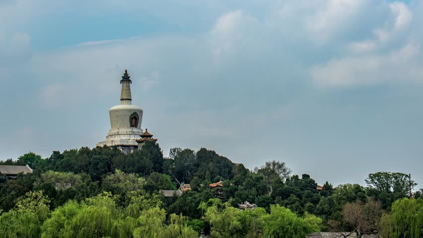 Time lapse view of White Pagoda rising above lush green trees in Beihai Park, Beijing, China against cloudy sky