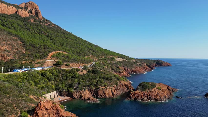 Panoramic aerial view of Esterel Mountains coastline with winding road, railway tracks and a passing train above the Mediterranean Sea, French Riviera, Southern France, dramatic cliffs