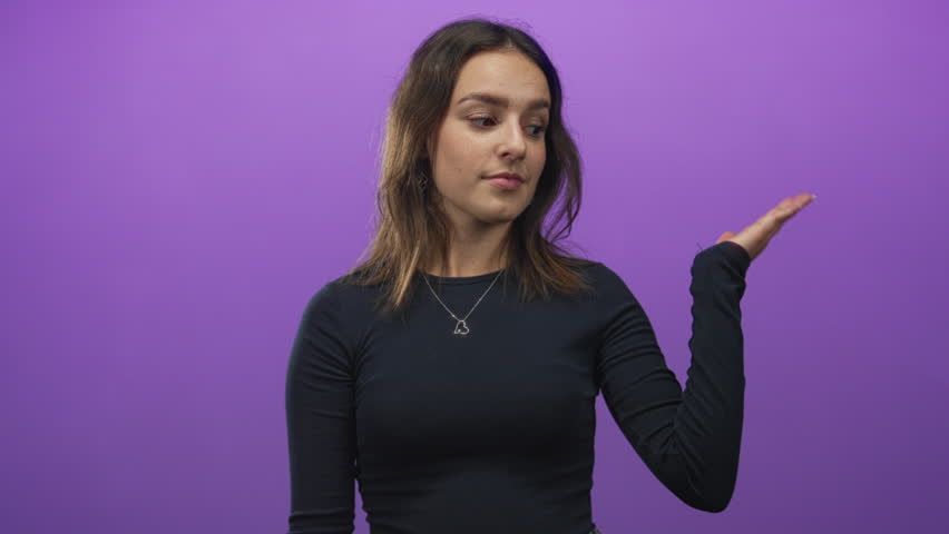 Young hispanic woman pointing finger to open palm while smiling in purple studio; product demo playful.