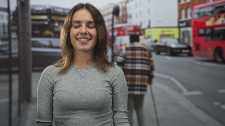 Woman smiling and standing with visible heart necklace and bare face framed by hair on a busy city street beside cars and a red bus, looking slightly right; confidence.