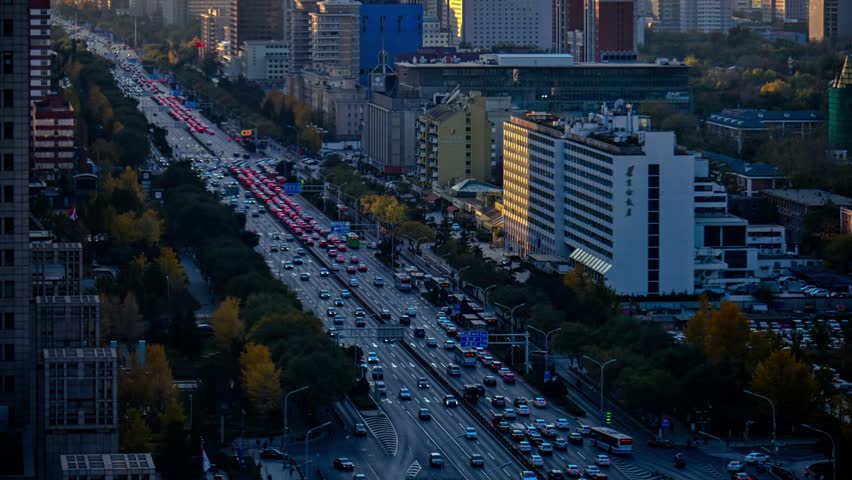 Heavy traffic congestion on Chang'an Avenue during rush hour in Beijing, China, with illuminated buildings and red brake lights creating urban evening scene.