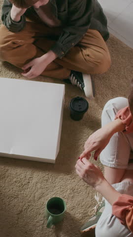 Vertical top view shot of hungry family of unrecognizable man, woman, and their son eating pizza on floor